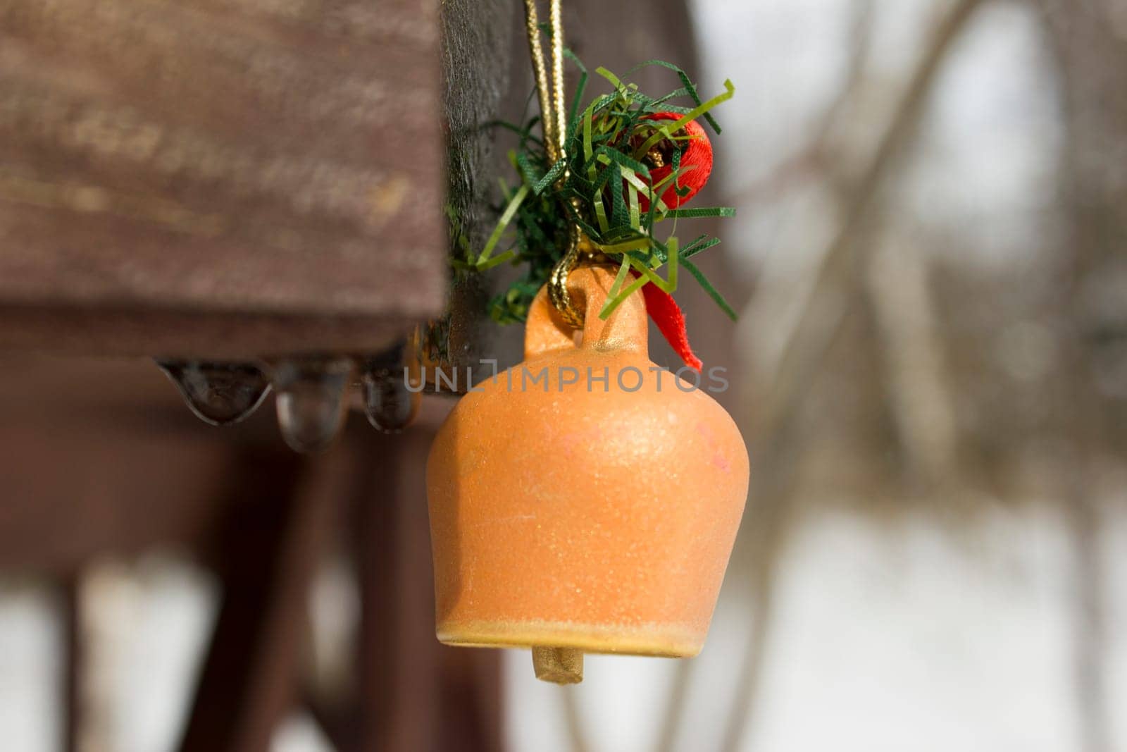 Toy bell pinned on a wooden frame with melting snow water drops running down.