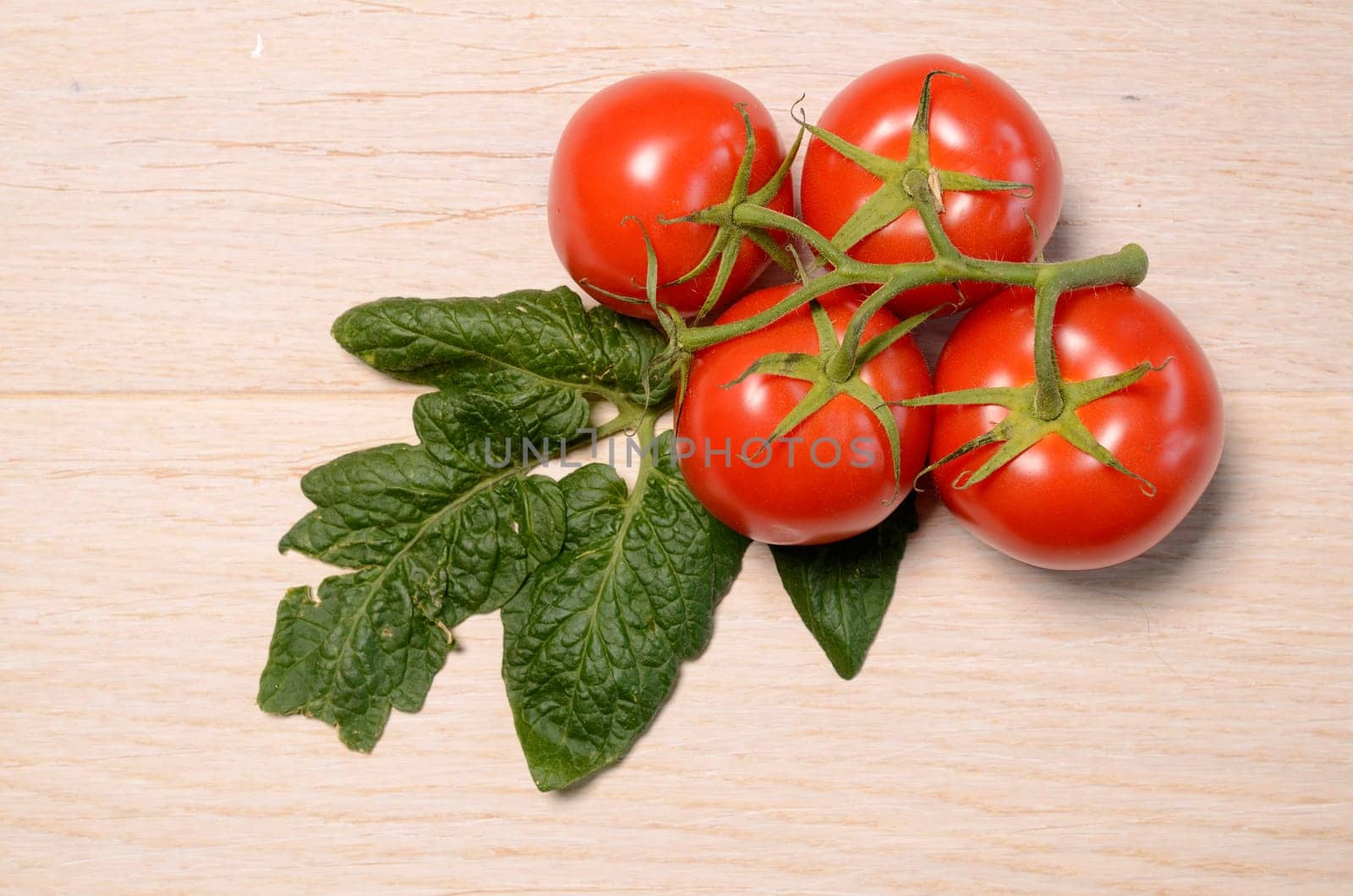 Four fresh tomatoes with a leaf on a wooden background