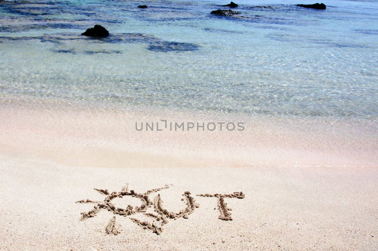 Word "OUT"" written on sand on a beautiful beach, blue waves in background"