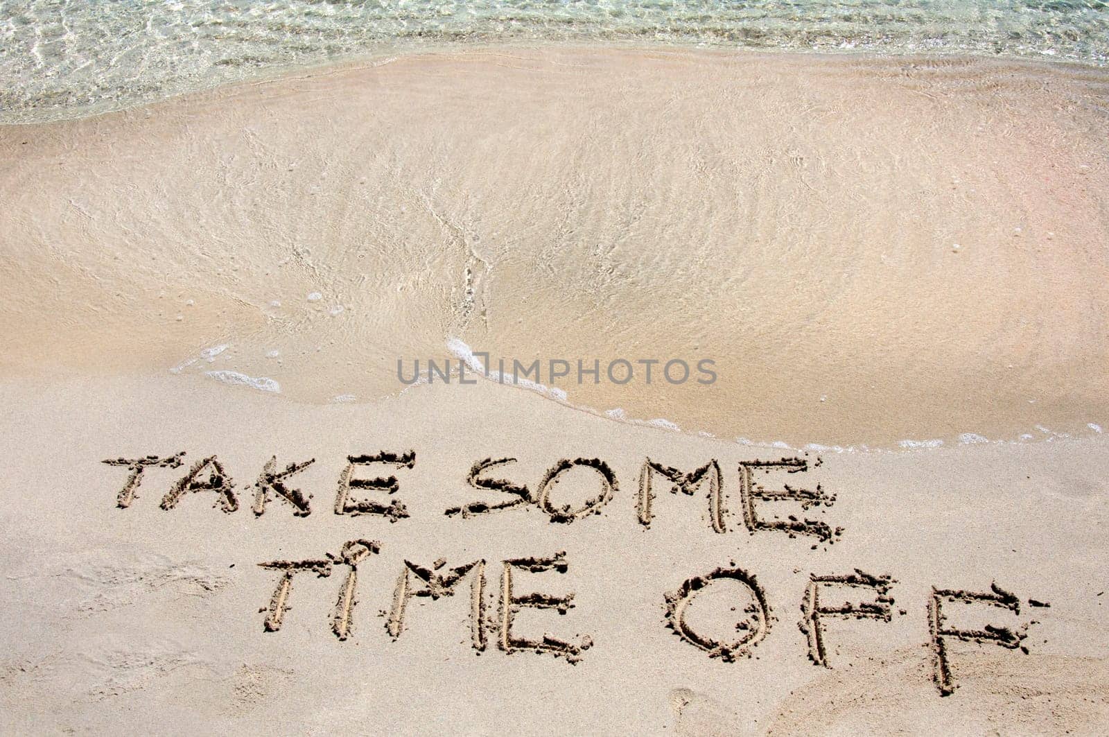 TAKE SOME TIME OFF written on sand on a beautiful beach, blue waves in background