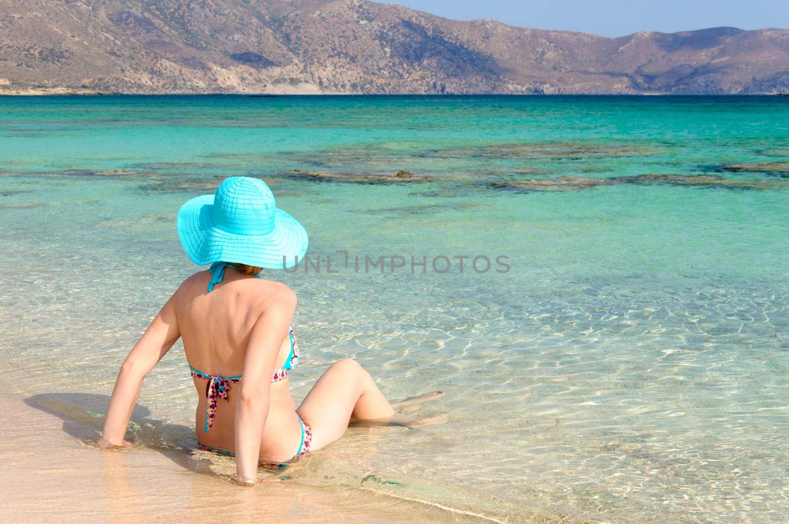 Beautiful young woman in bikini with sunhat, relaxing on the sunny beach. Relaxing concept