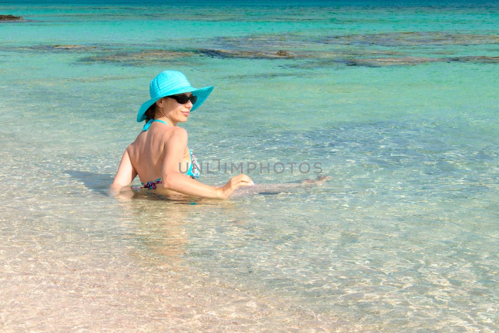 Beautiful young woman in bikini with sunhat, relaxing on the sunny beach. Relaxing concept