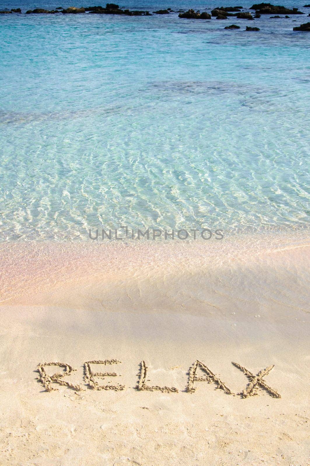 Relax word written in the sand, on a beautiful beach with clear blue waves in  background