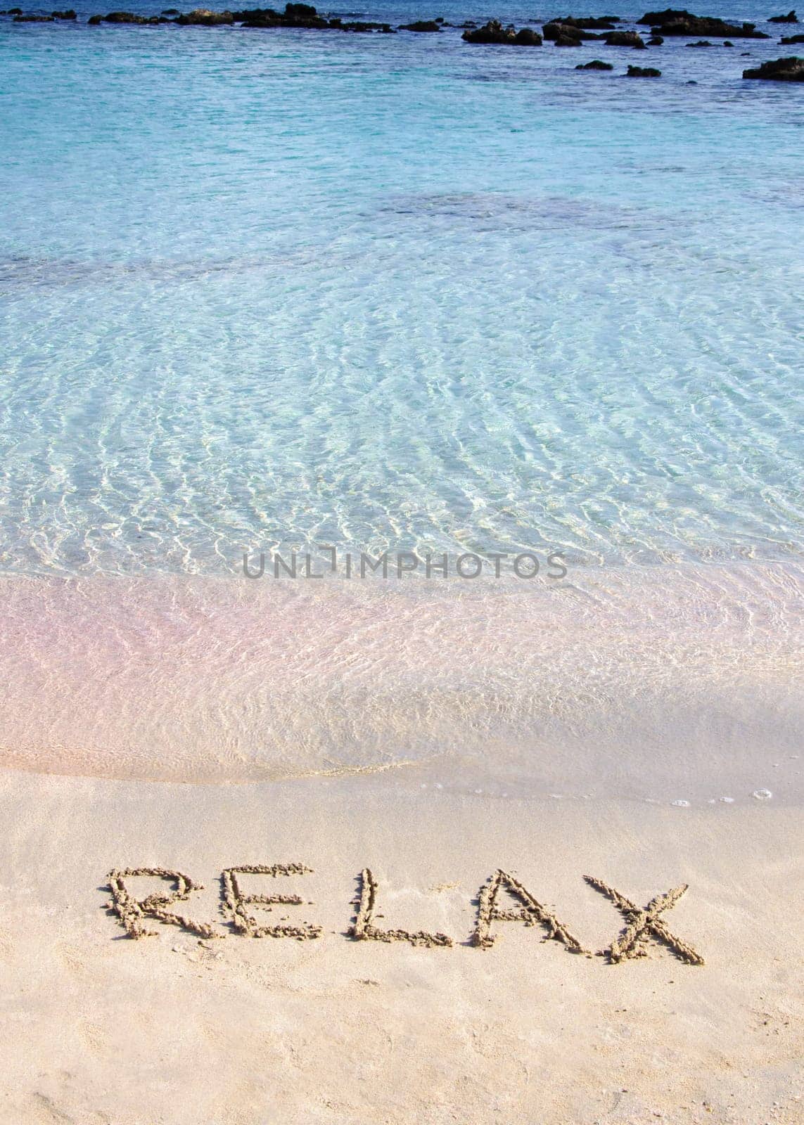 Relax word written in the sand, on a beautiful beach with clear blue waves in  background