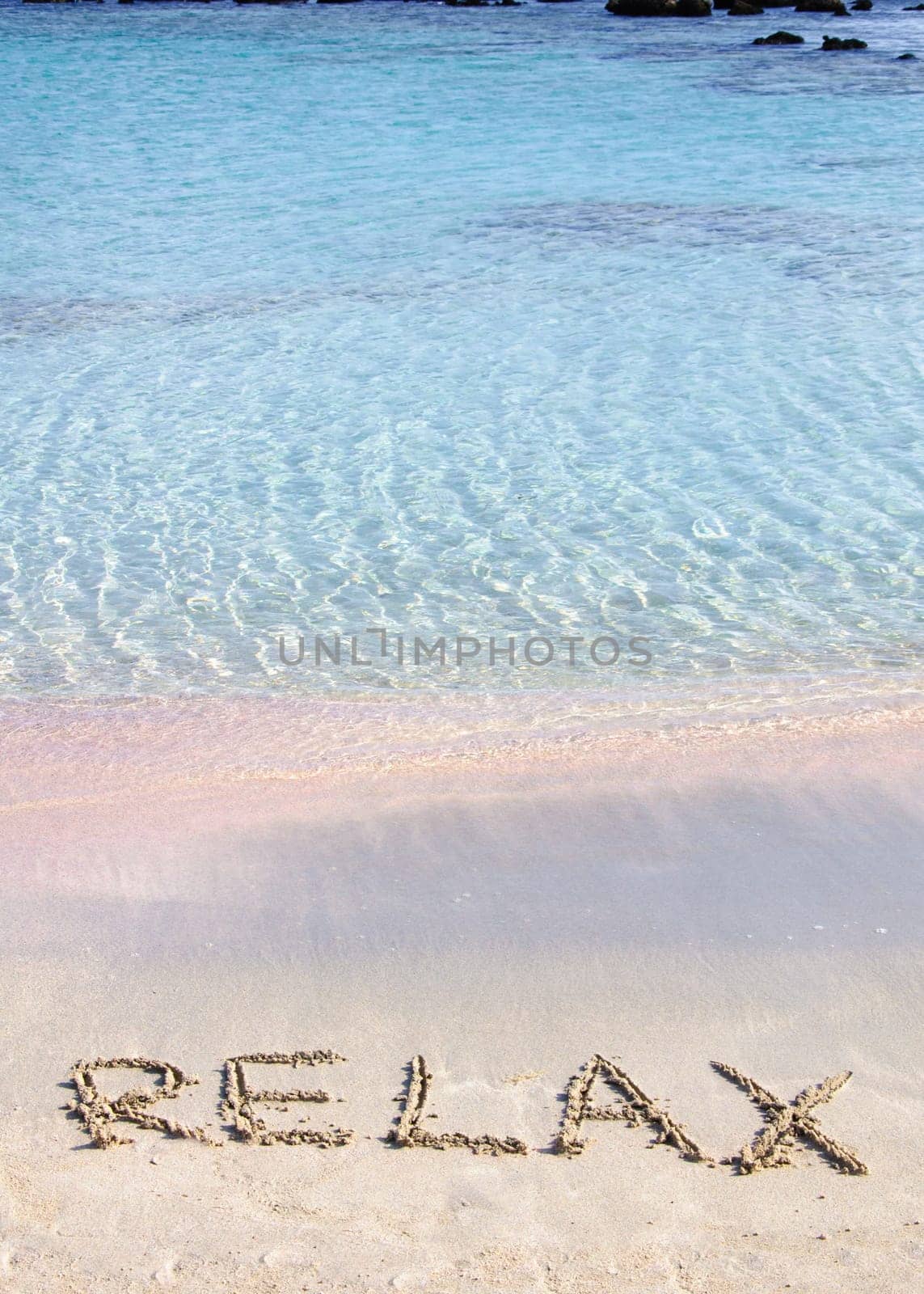 Relax word written in the sand, on a beautiful beach with clear blue waves in  background