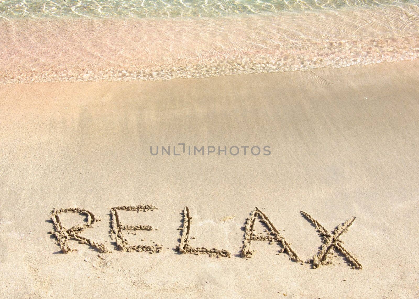 Relax word written in the sand, on a beautiful beach with clear blue waves in  background