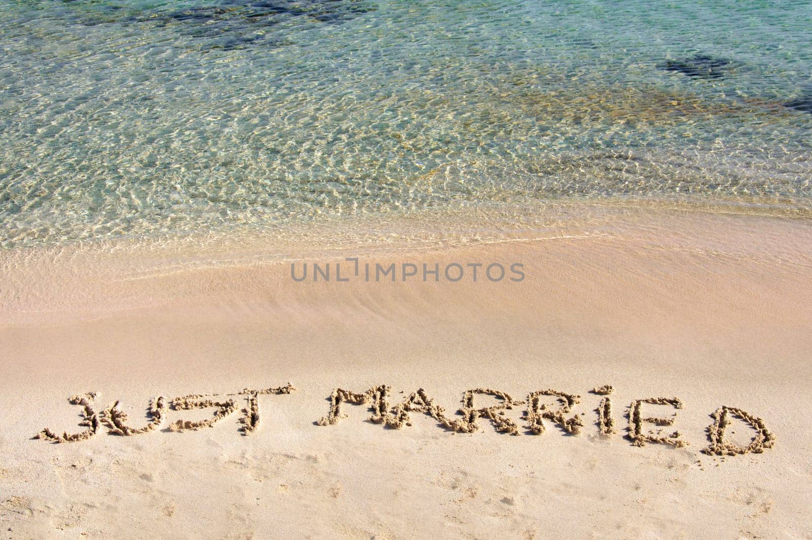 Just Married written in sand on a beautiful beach, blue clear waves in background