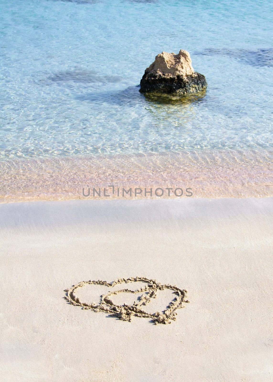 Two hearts drawn in the sand on a beautiful beach, with waves in background