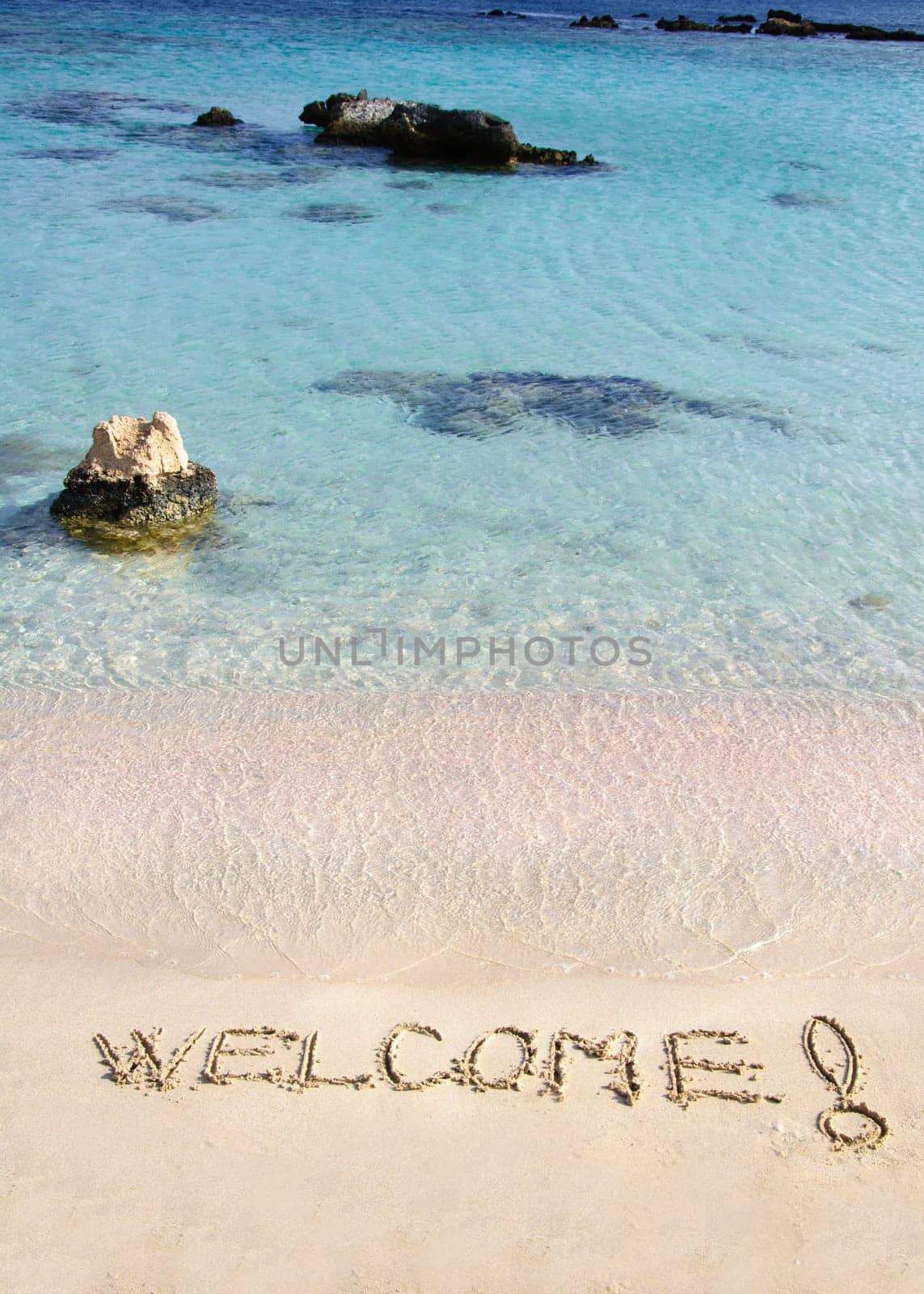 Welcome message written on white sand, with tropical sea waves in  background
