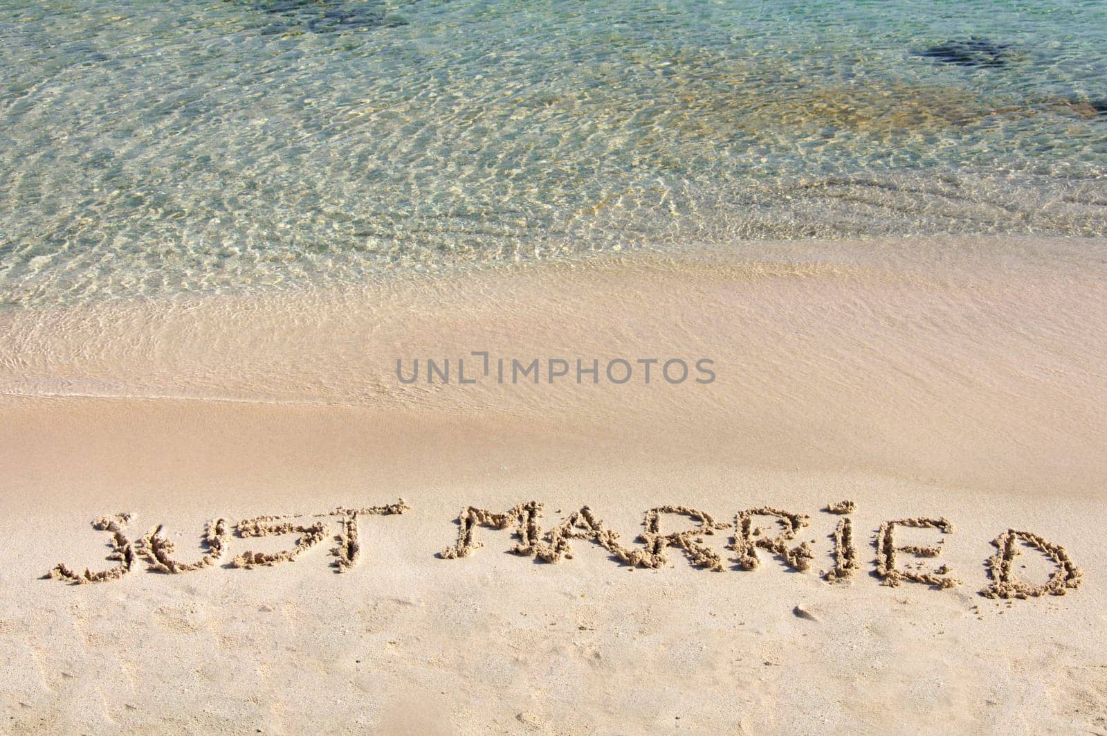 Just Married written in sand on a beautiful beach, blue clear waves in background