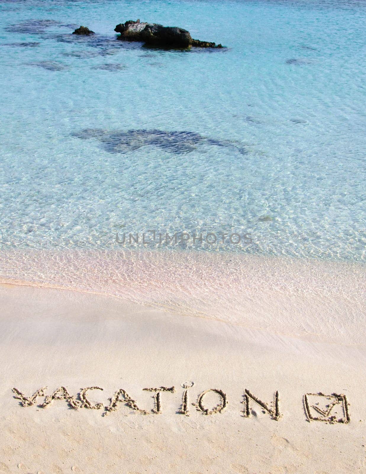 Vacation and checked mark written on sand on a beautiful beach, blue waves in background