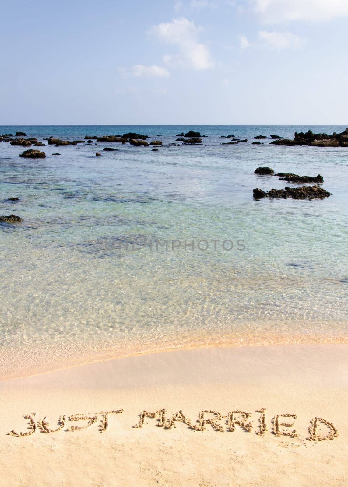 Just Married written in sand on a beautiful beach, blue clear waves in background