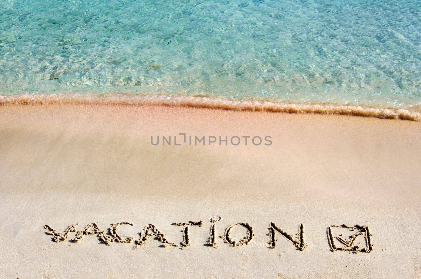 Vacation and checked mark written on sand on a beautiful beach, blue waves in background