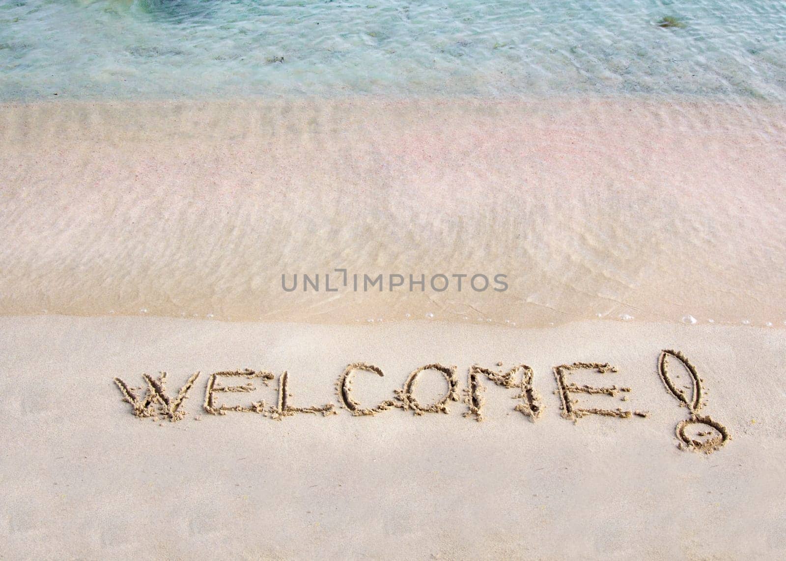 Welcome message written on white sand, with tropical sea waves in  background