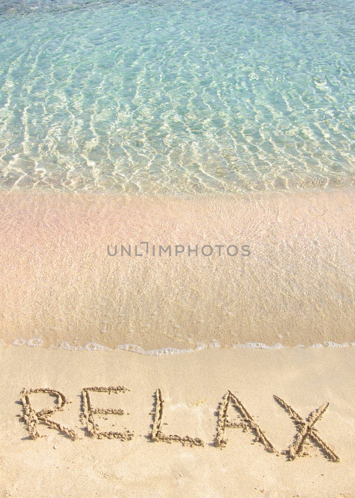 Relax word written in the sand, on a beautiful beach with clear blue waves in  background