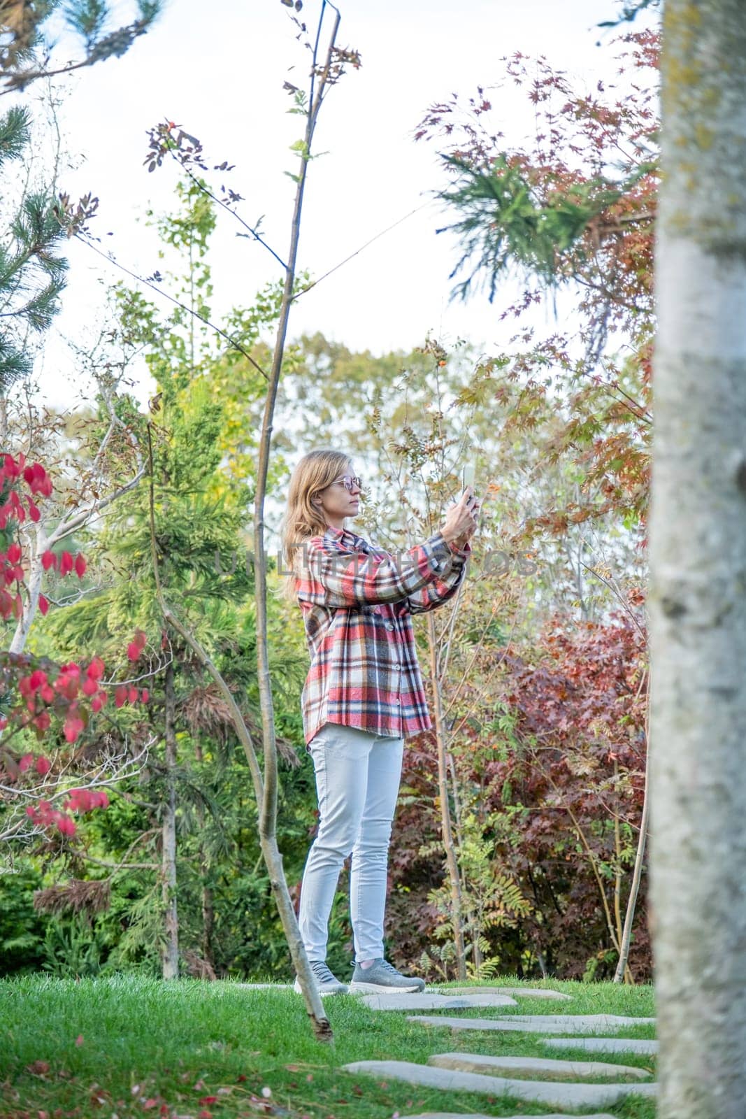 Woman in red plaid shirt enjoying nature standing in Japanese Garden taking photo on smartphone