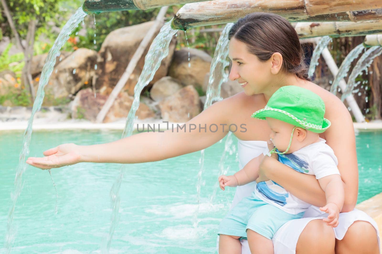 Baby and mother are sitting on the edge of a pool