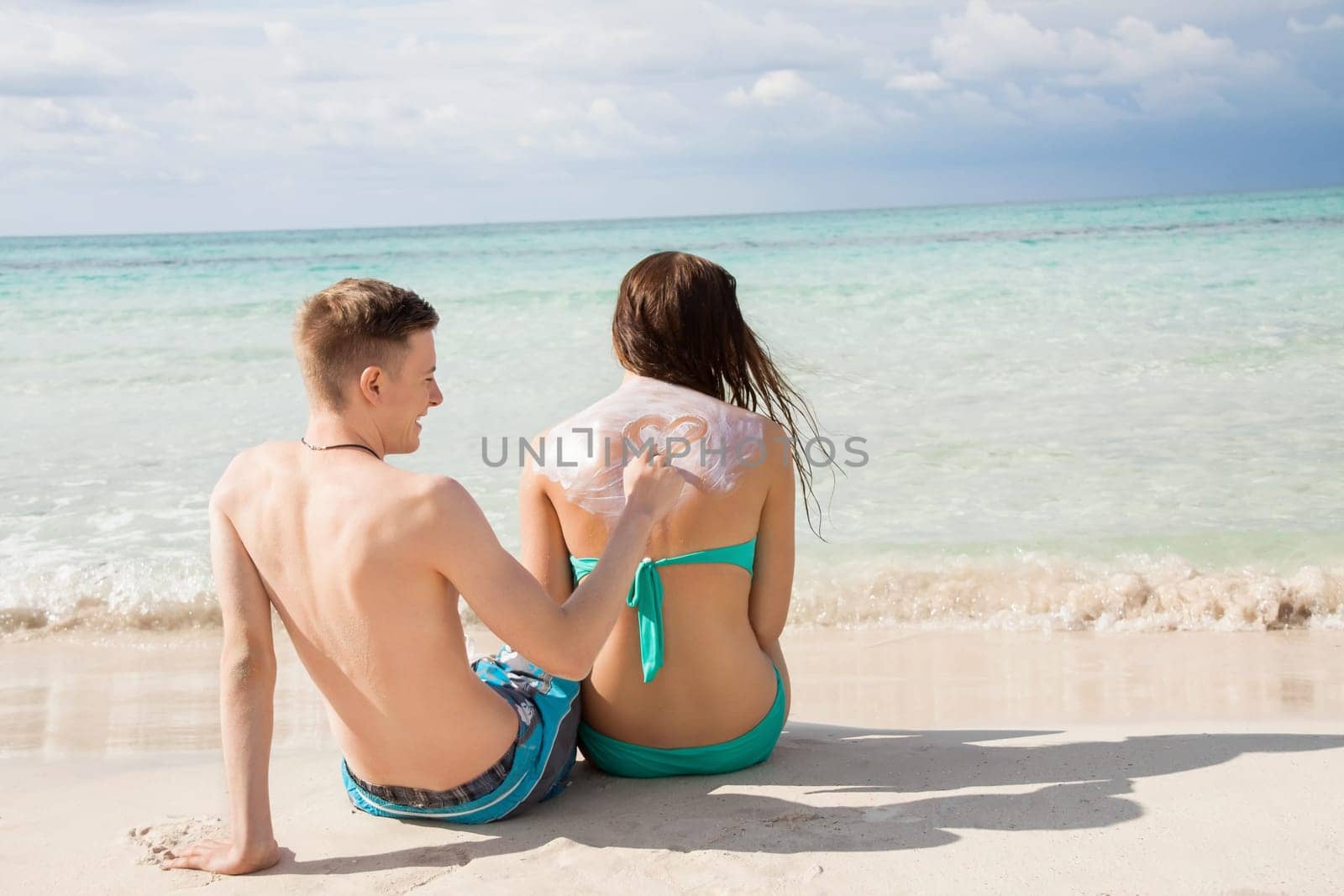 Young couple in love on the beach sun protection care leisure in summer holiday love sunscreen heart painting