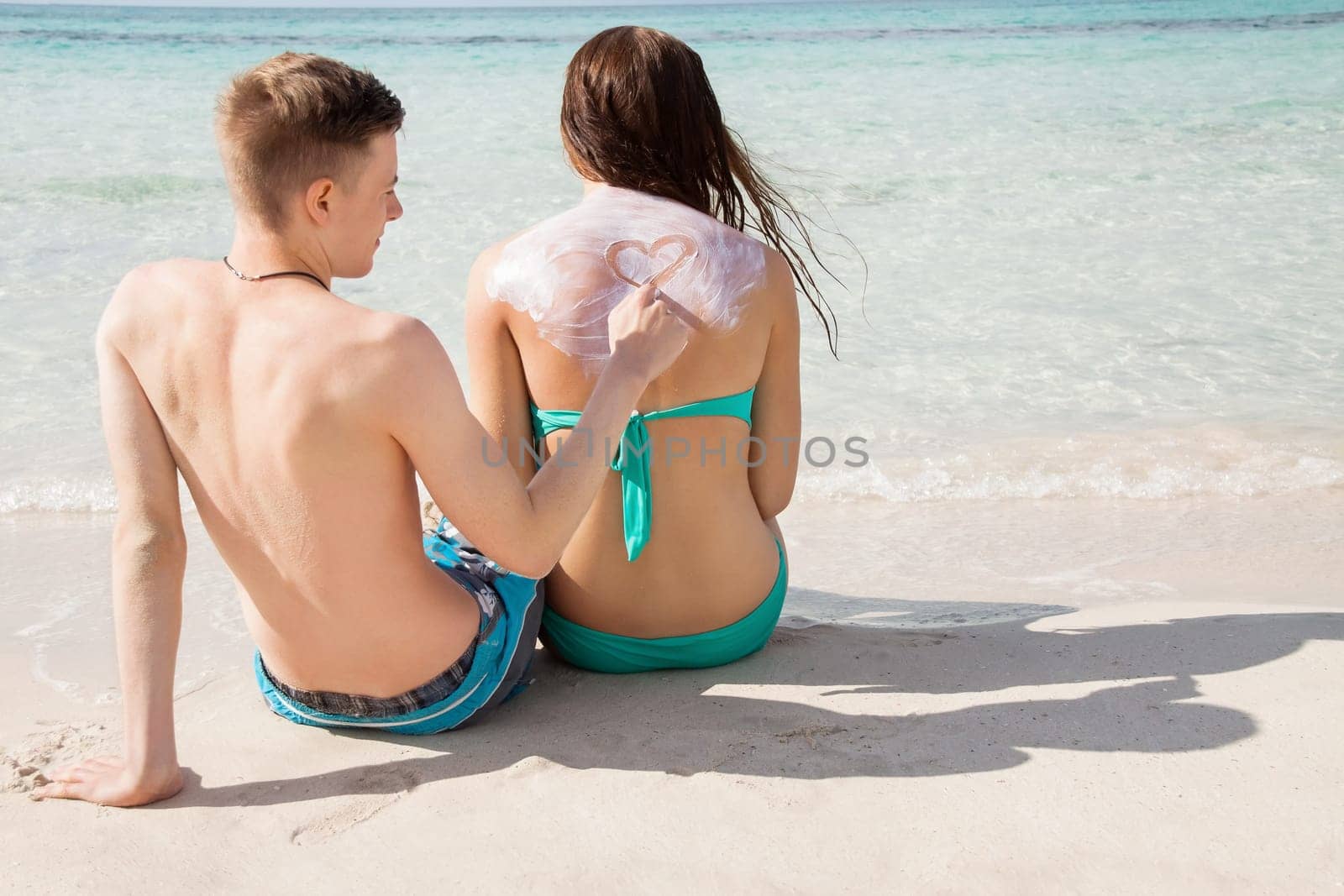 Young couple in love on the beach sun protection care leisure in summer holiday love sunscreen heart painting