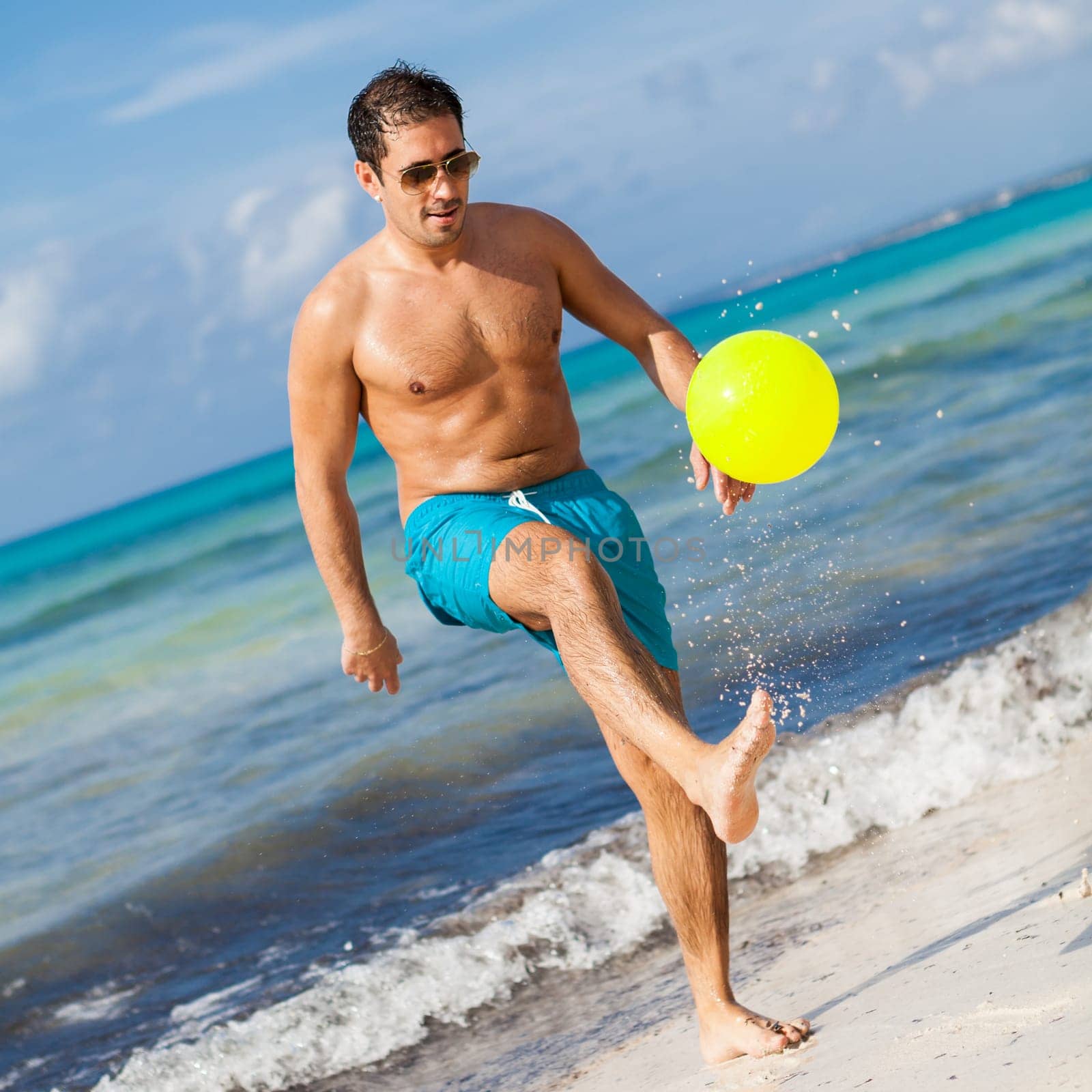 Young laughing man plays ball Football on the beach in summer holiday leisure