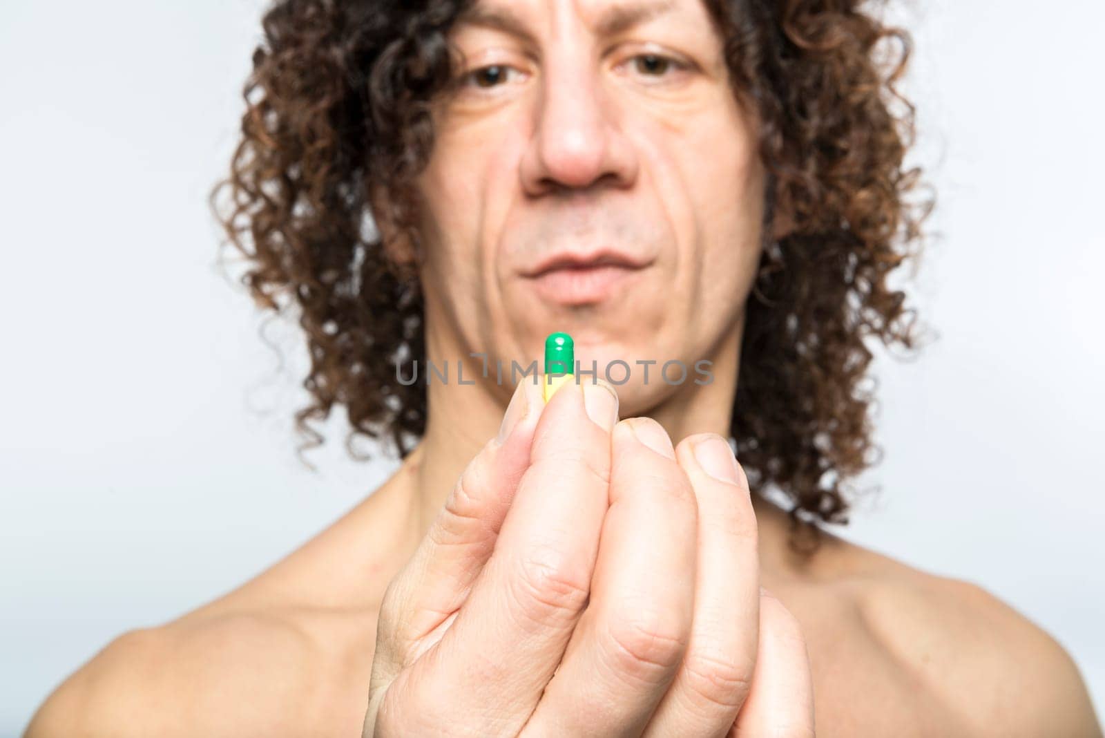 Cropped shot of bare chested mediterranean man holding colourful pill