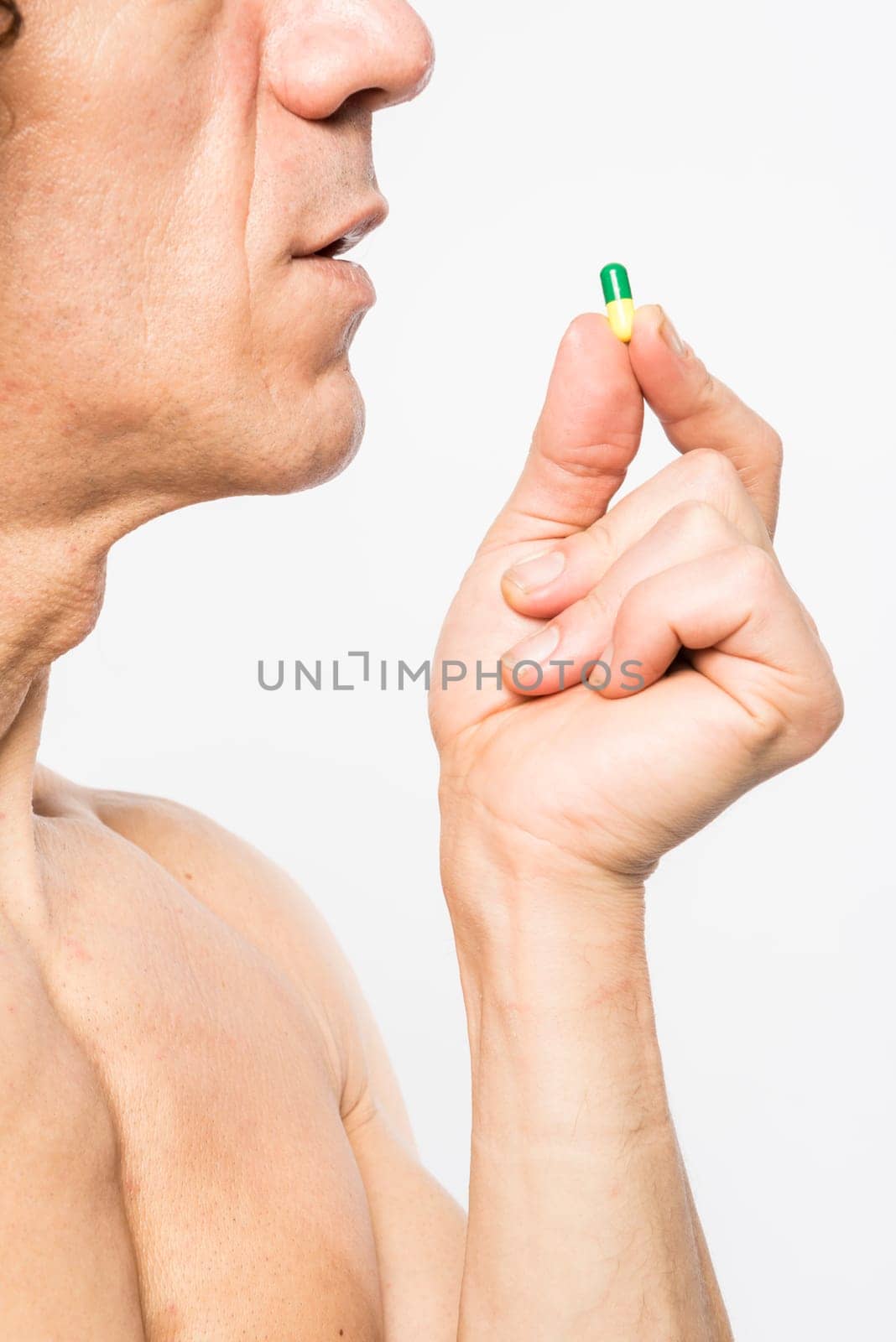 Cropped shot of bare chested mediterranean man taking colourful pill
