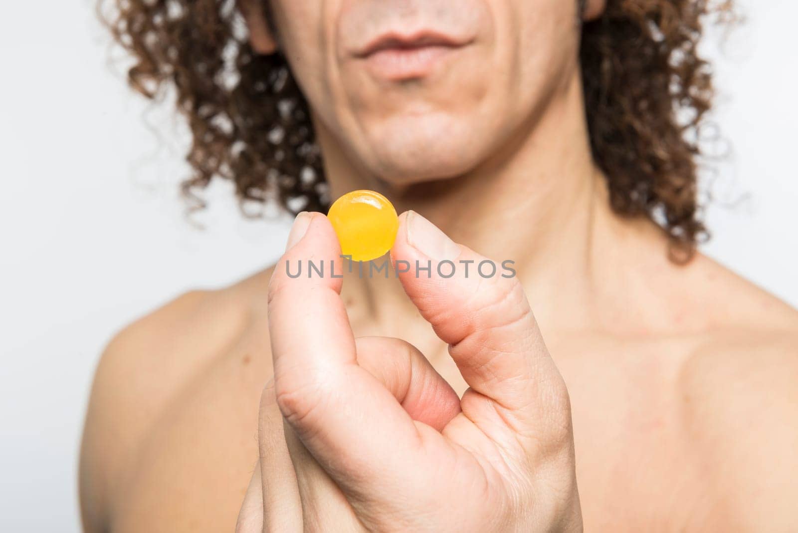 Cropped shot of bare chested mediterranean man holding colourful pill