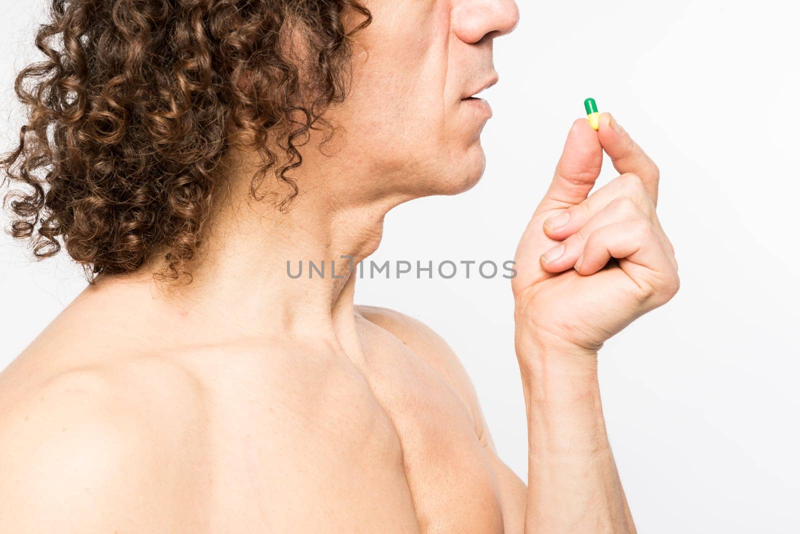 Cropped shot of bare chested mediterranean man taking colourful pill