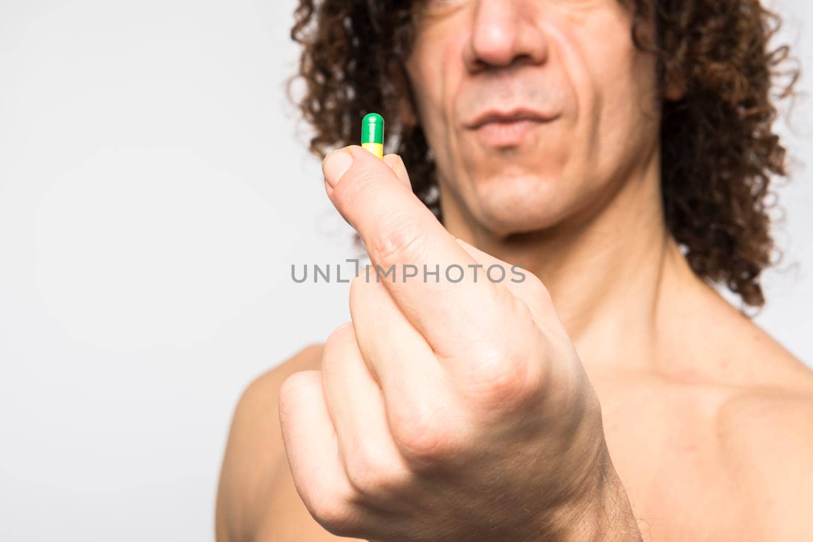 Cropped shot of bare chested mediterranean man holding colourful pill