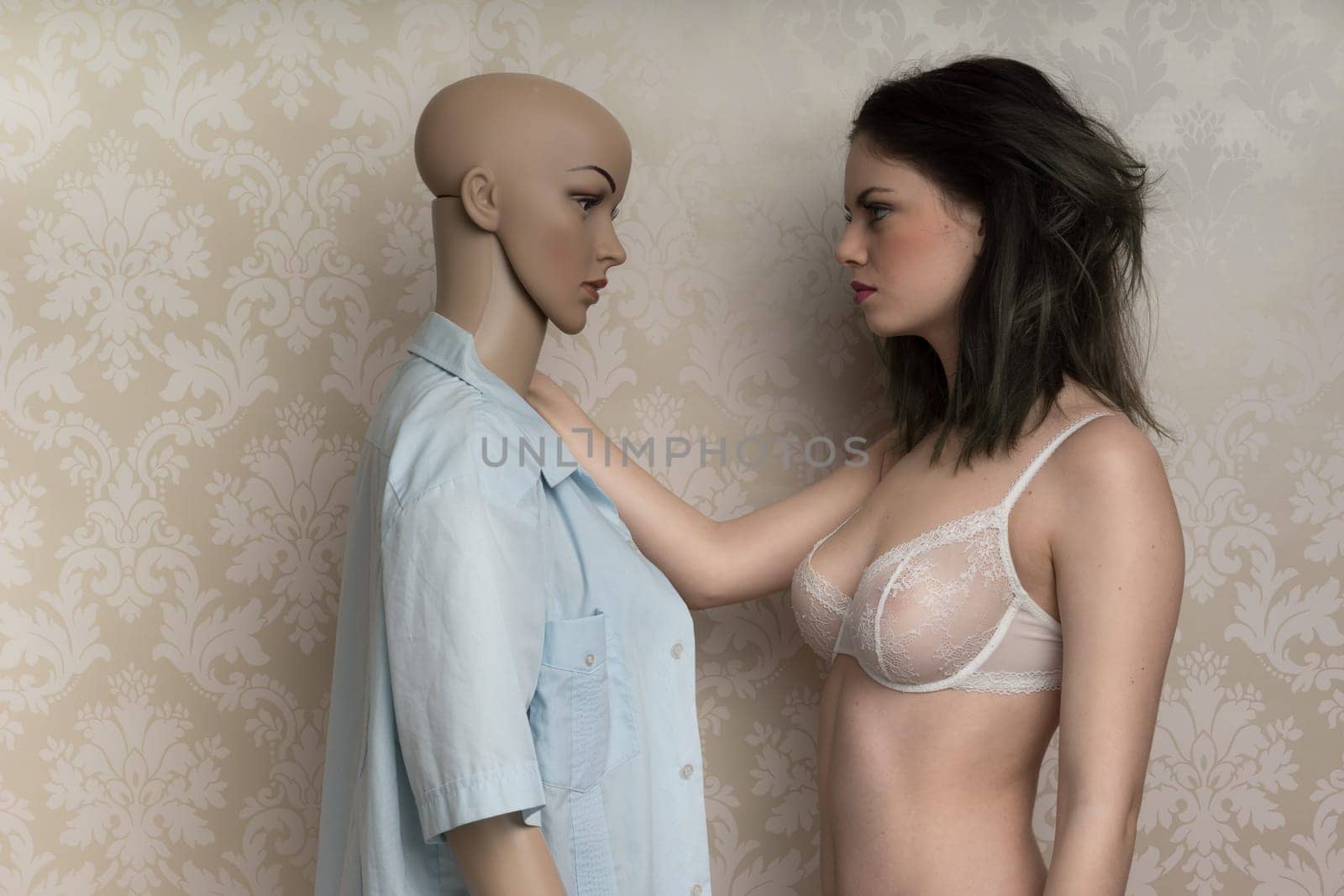 Beautiful young model with a mannequin standing face to face as she models a sexy see-through bra