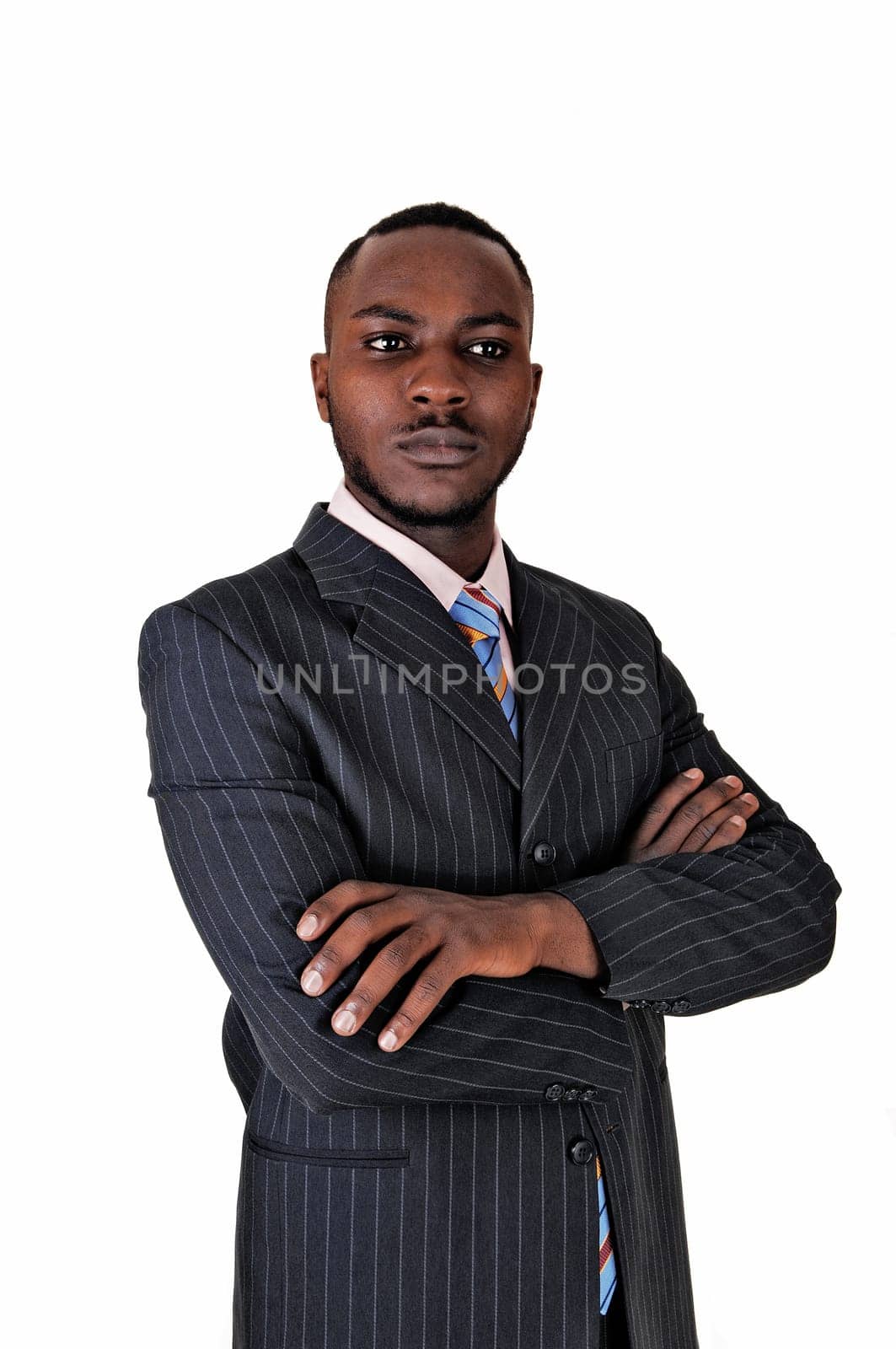 A young black business man standing in a suit and tie, with his arms.crossed for white background..