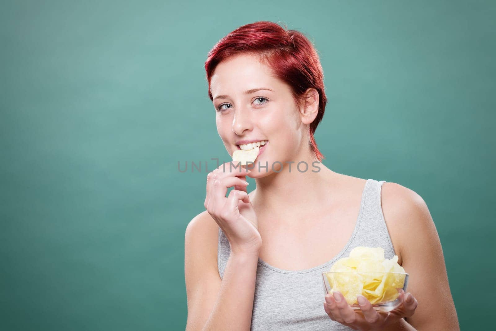 Young happy red-haired woman nibbles on potato chips