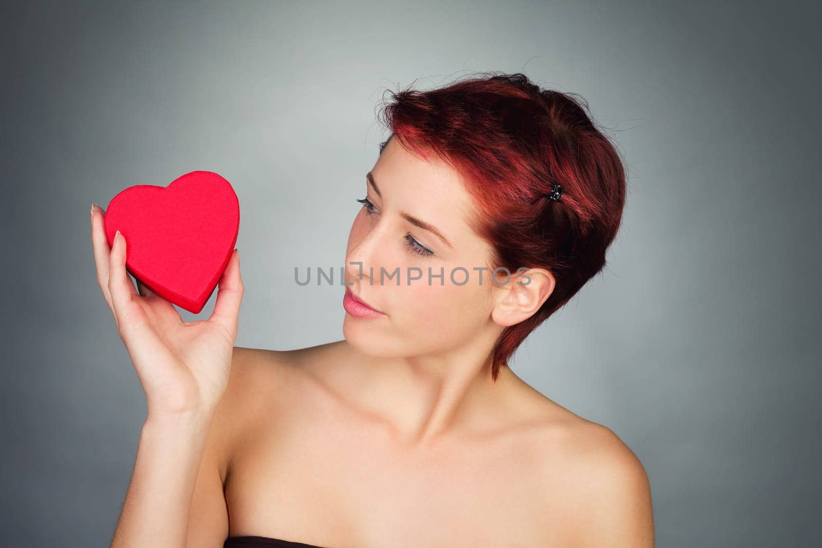 Young red-haired woman looks at a red heart in her hand