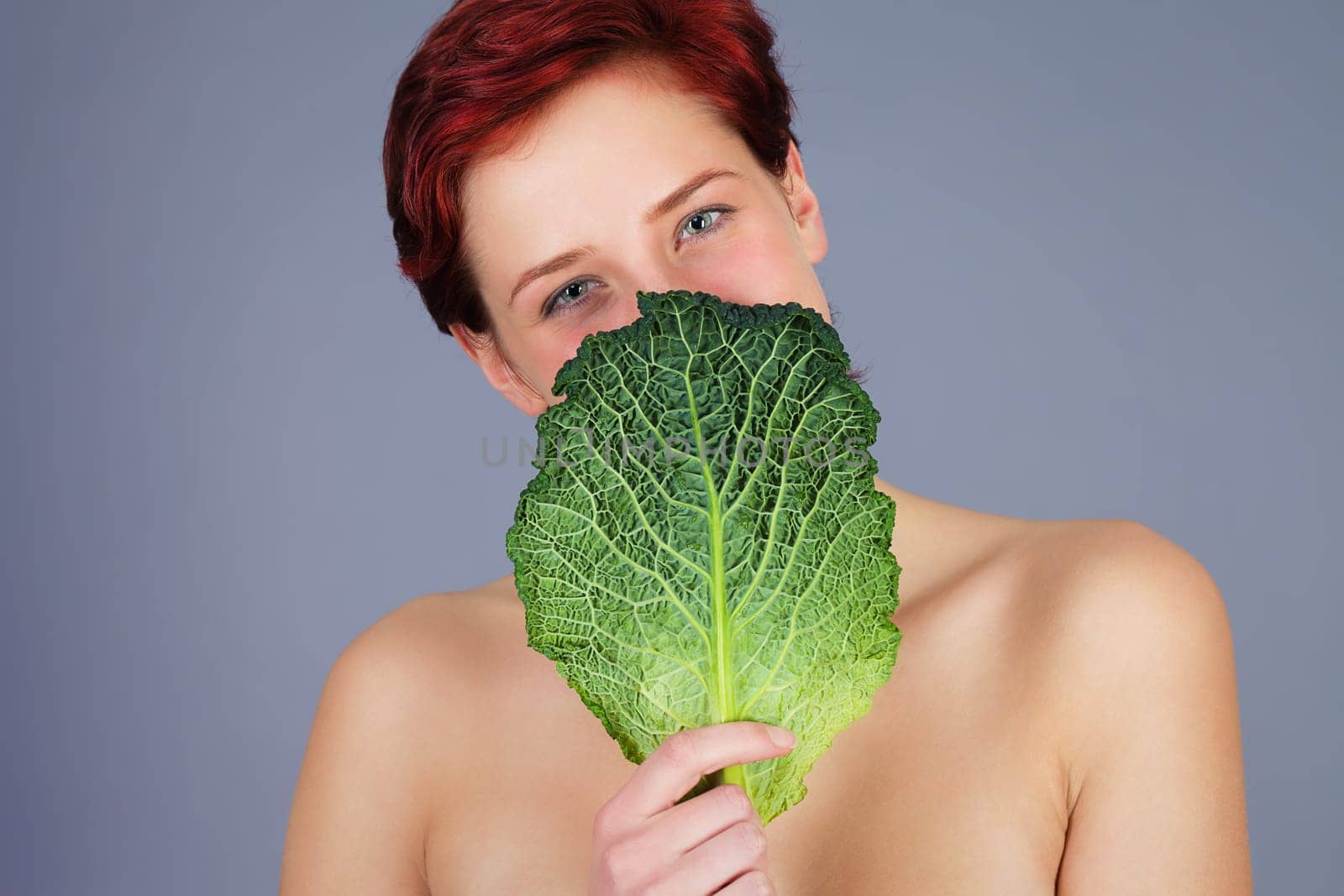 Young happy red-haired woman holds a leaf of savoy cabbage in front of her face