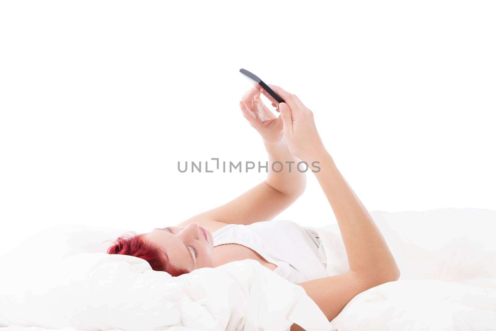 Young woman texting in bed against a white background