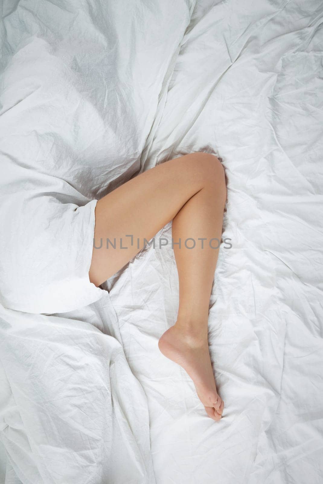 Beautiful leg of a woman in bed peeks out from under the sheet