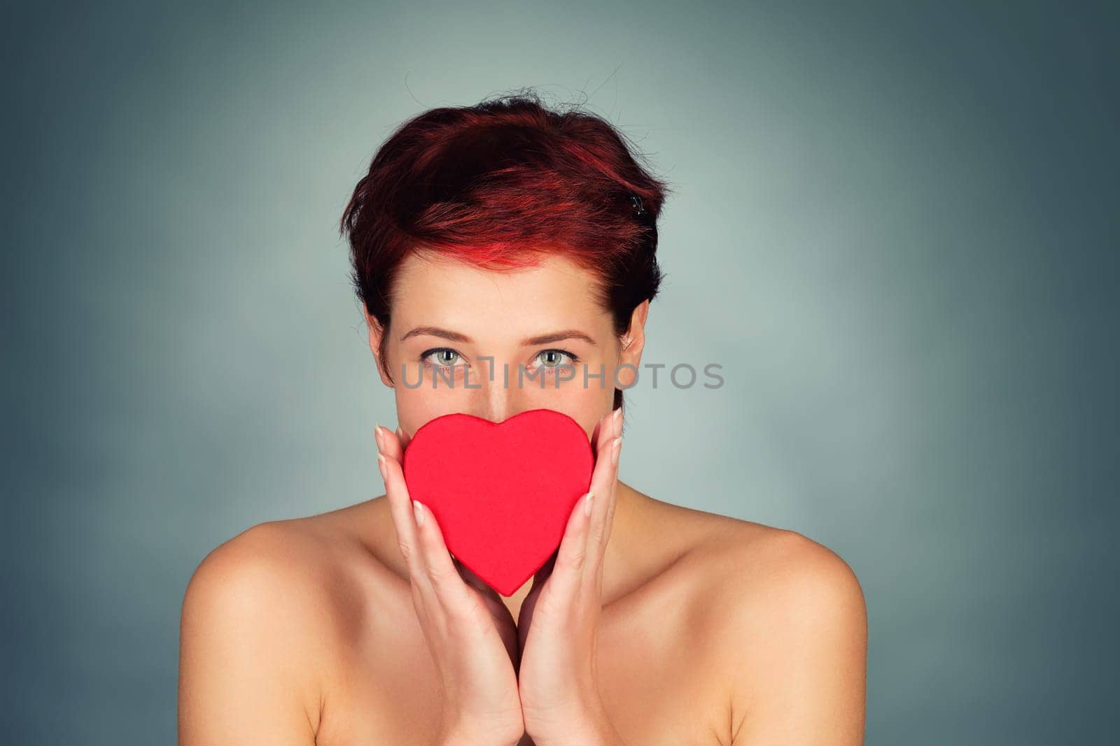 Young red-haired beautiful woman holds red heart in front of her face