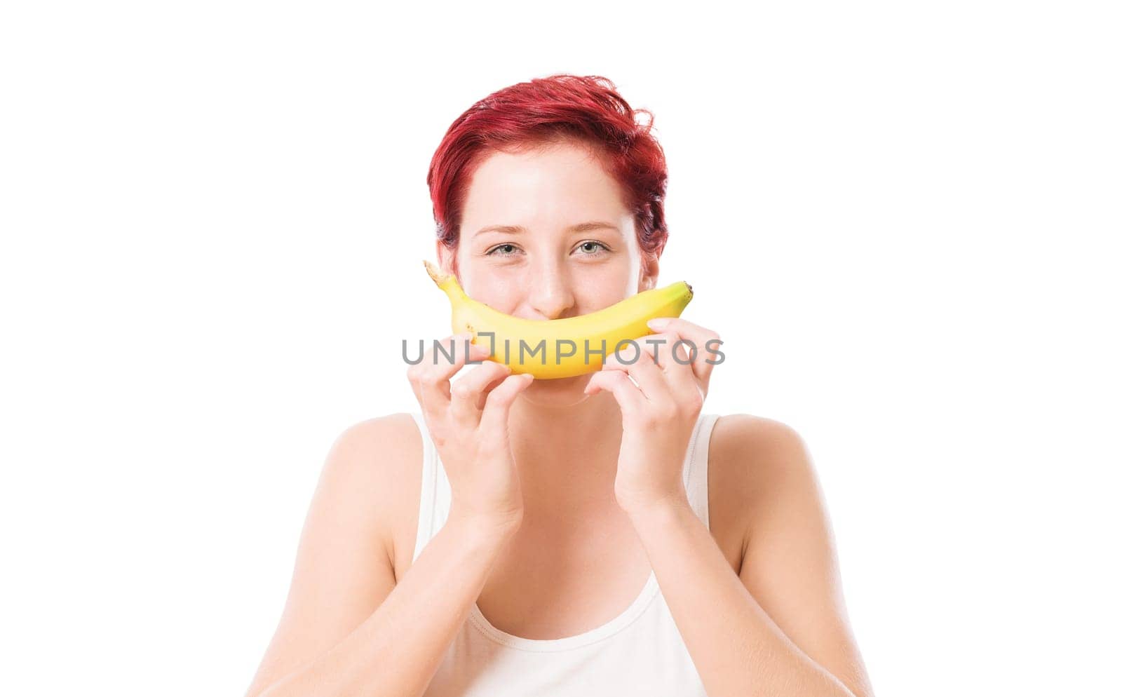 Young woman holds banana as a smile in front of her mouth against a white background