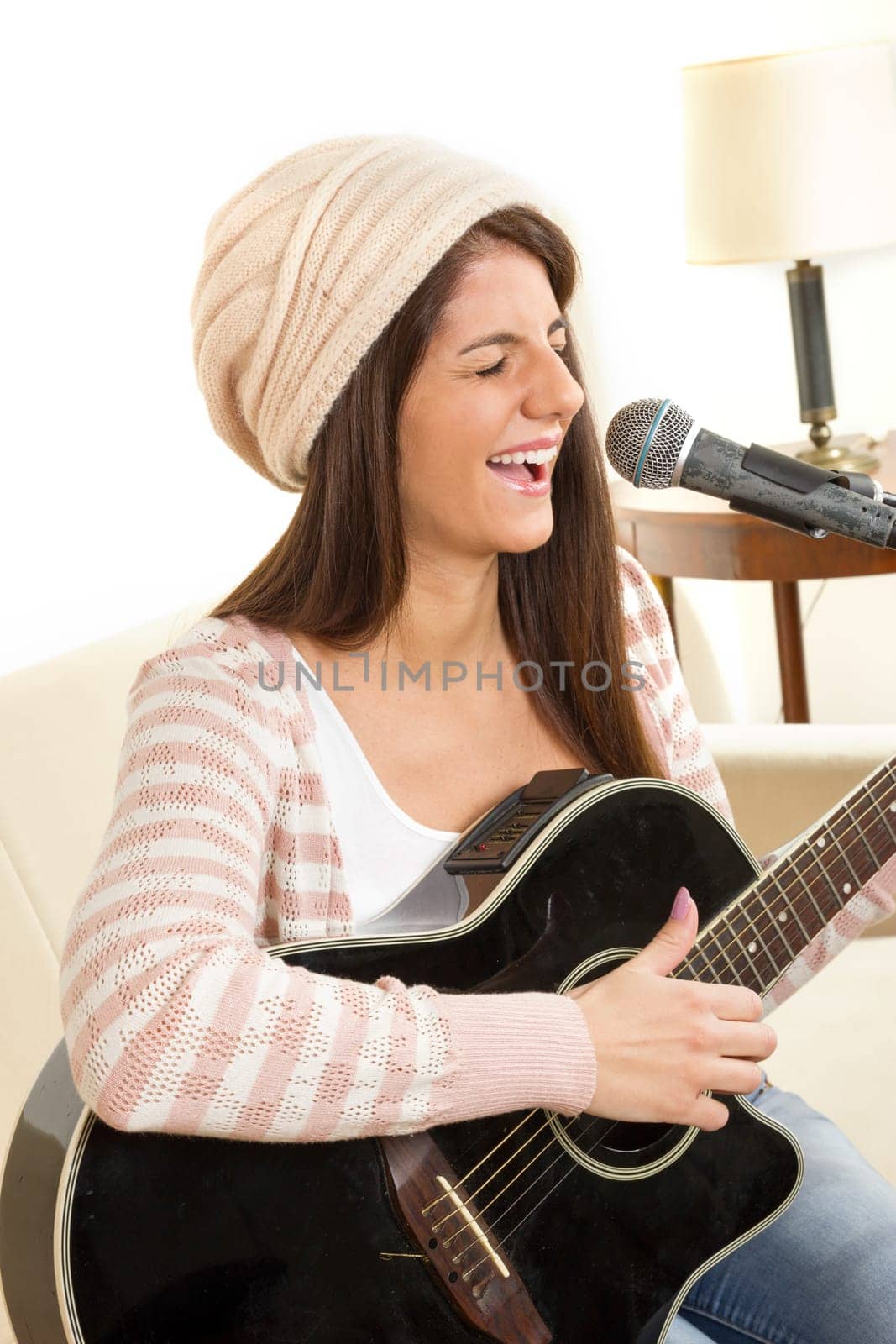 girl with cap playing a guitar and singing on microphone