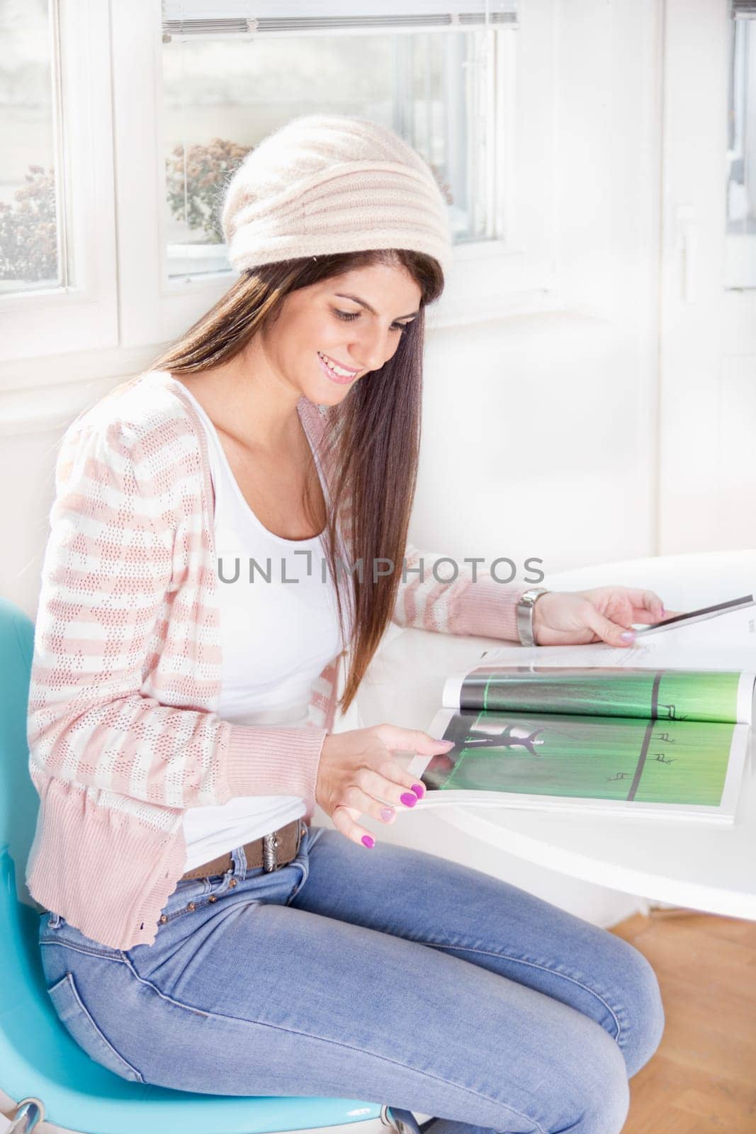 sweet girl wearing sweater and cap by the window with magazine