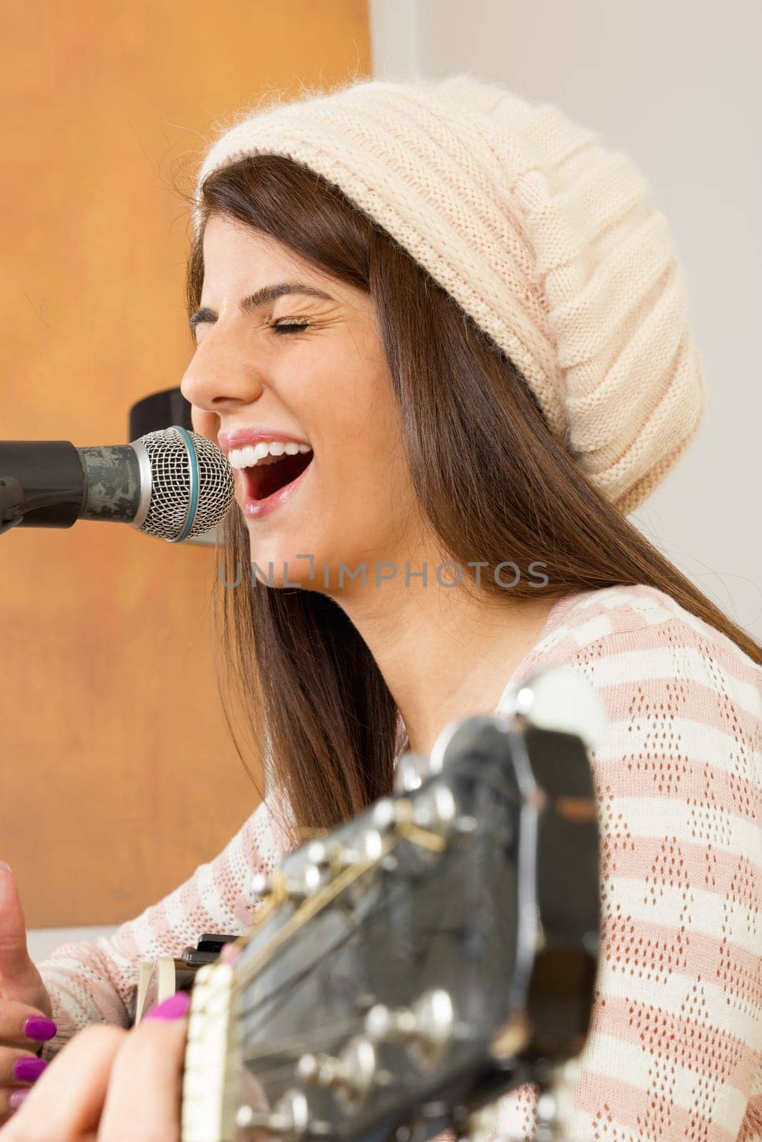 girl singing loud with effort and playing guitar wearing cap