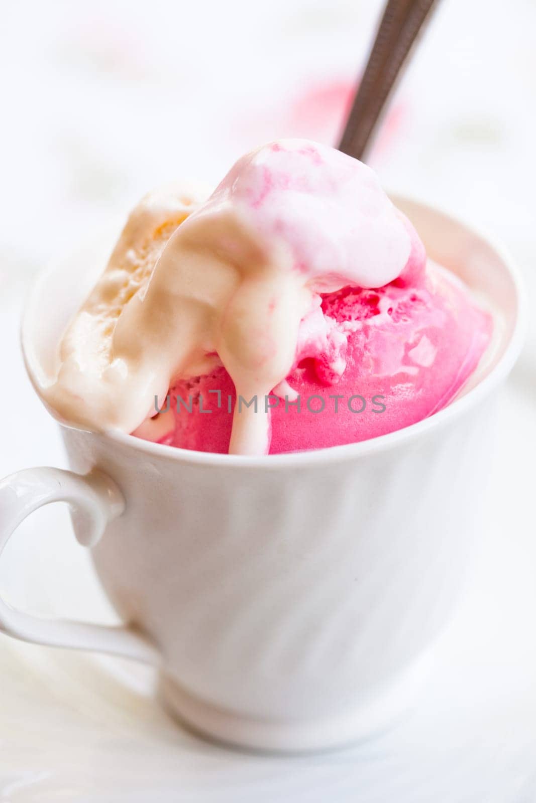 Closeup of cup with raspberry and vanilla ice cream and spoon on light background