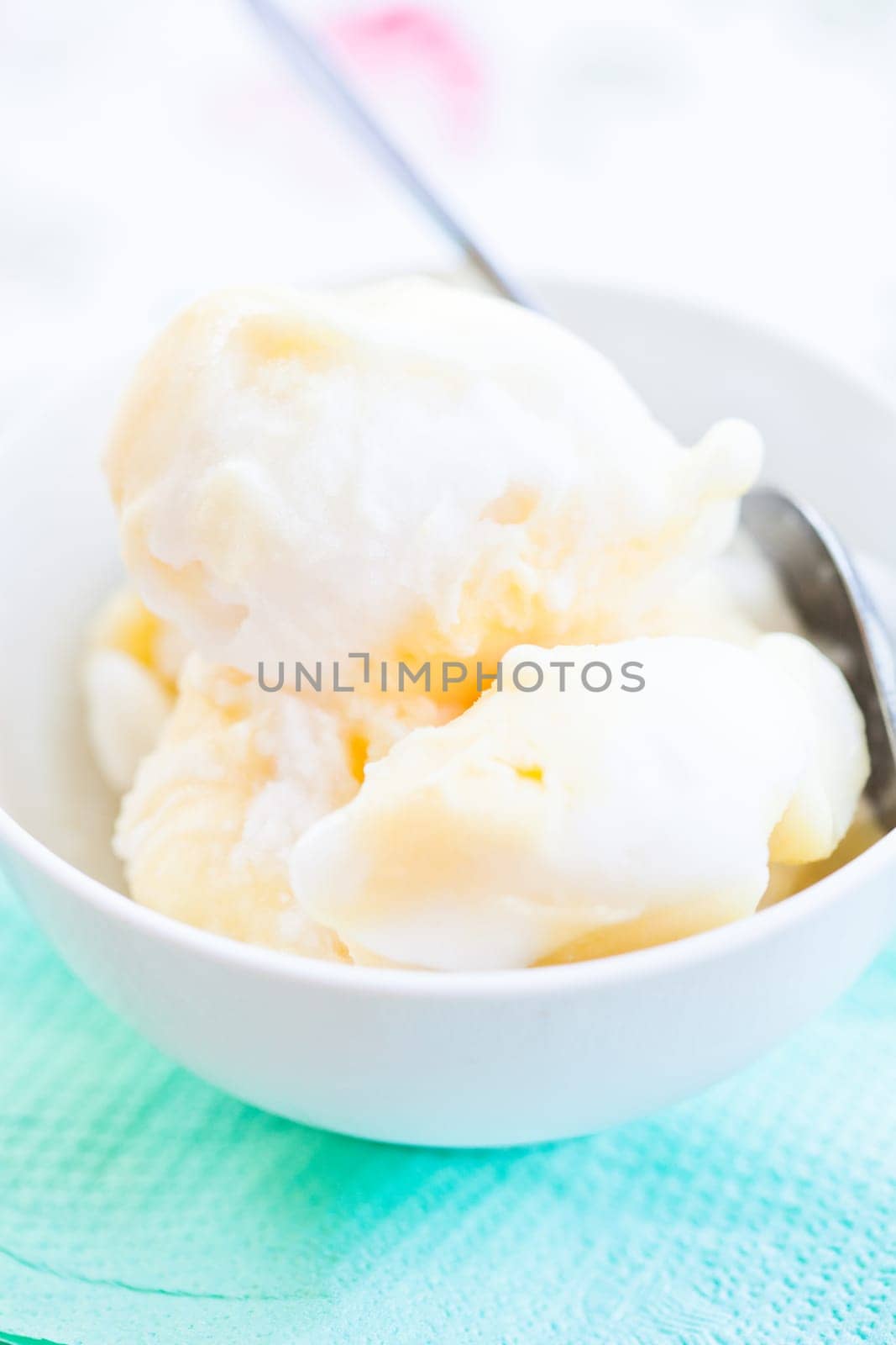 Closeup of scoops of vanilla ice cream and spoon in white bowl on light background