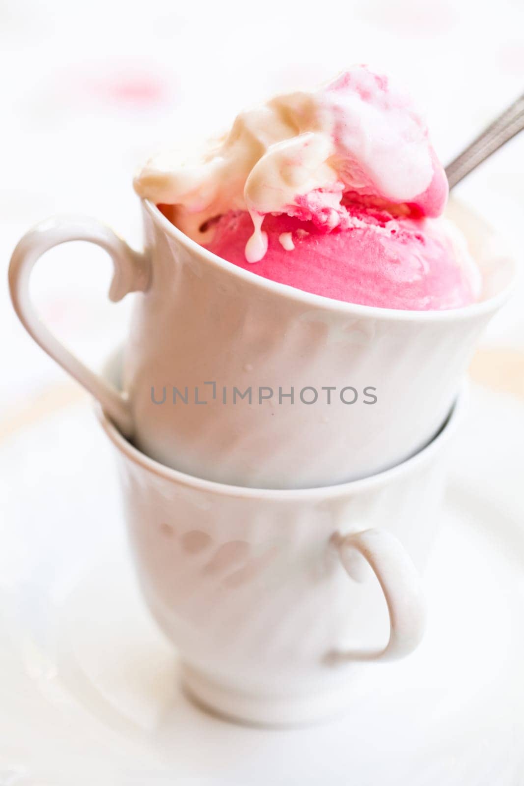 Closeup of cup with raspberry and vanilla ice cream and spoon on light background