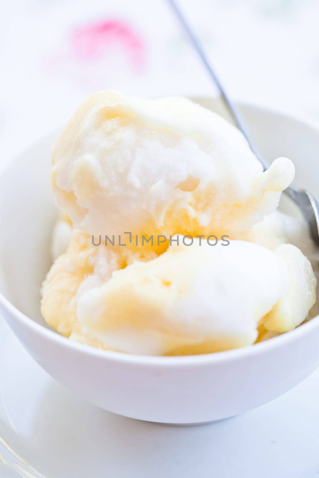 Closeup of scoops of vanilla ice cream and spoon in white bowl on light background