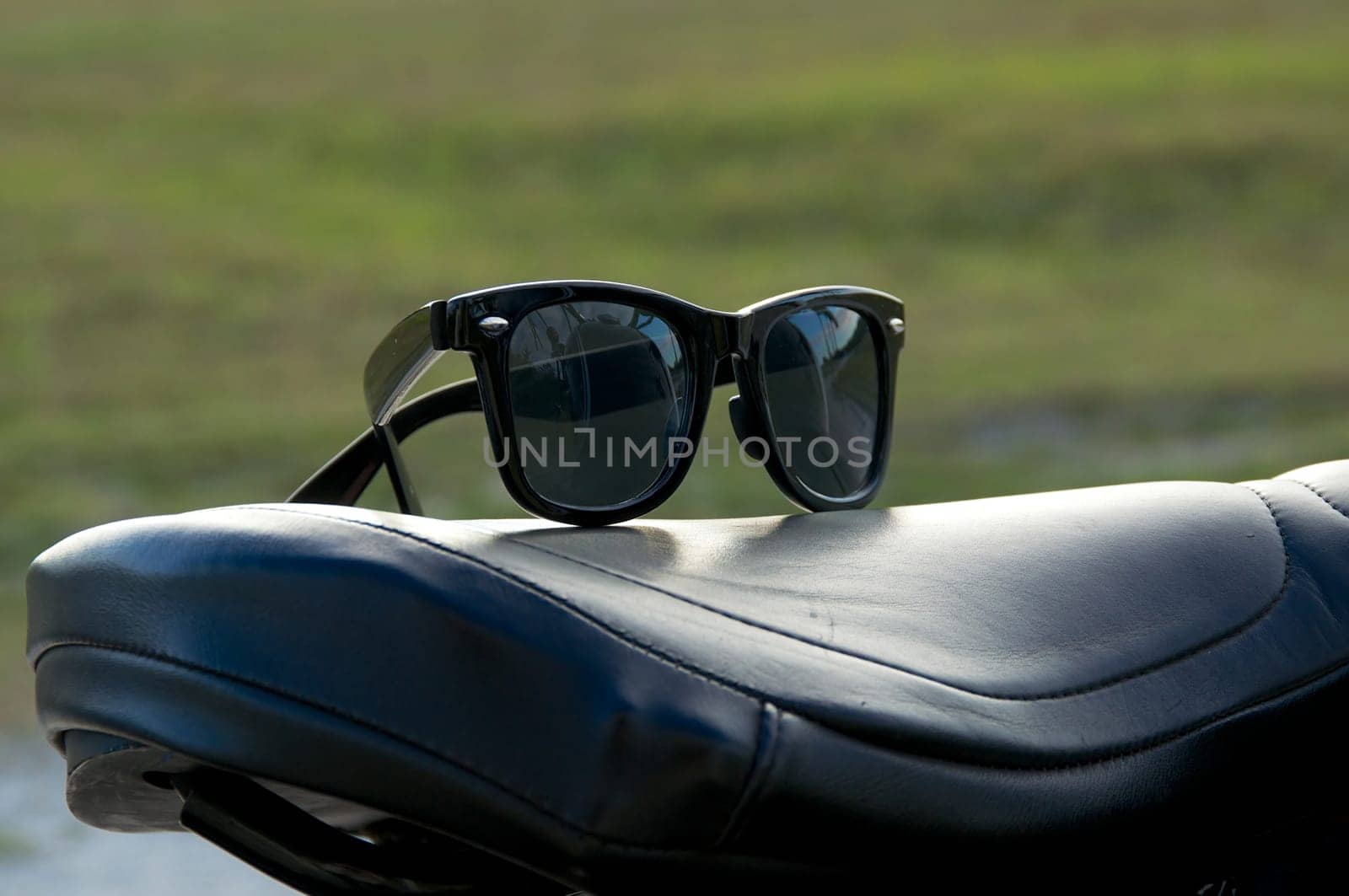 A pair of generic wayfarer sunglasses are on top of leather motorcycle seat. NOTE