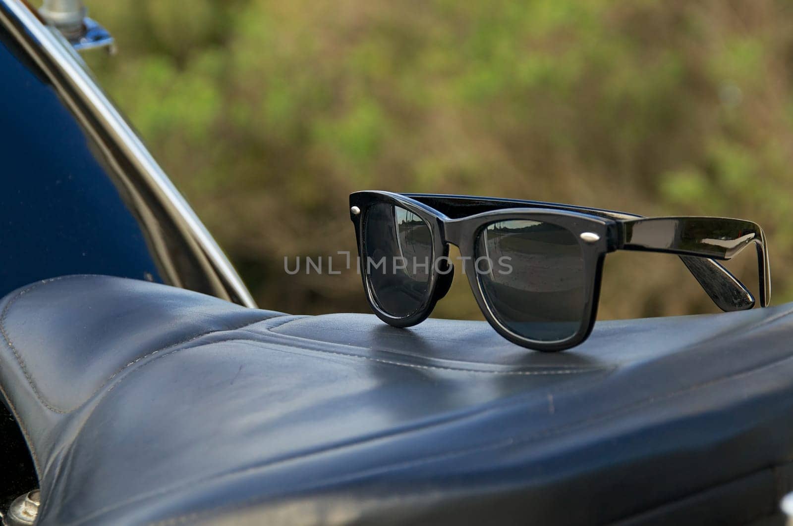 A pair of generic wayfarer sunglasses are on top of leather motorcycle seat. NOTE