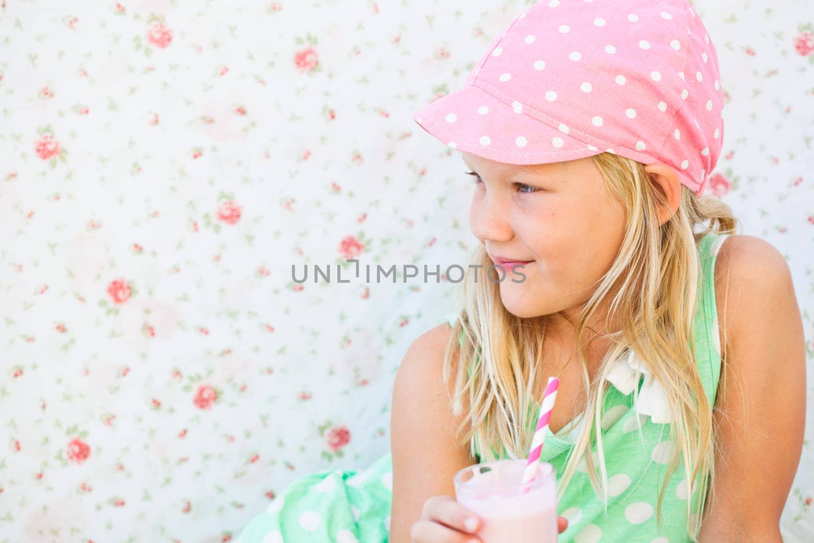 Smiling young girl holding milk fruit smoothie in glass with striped straw