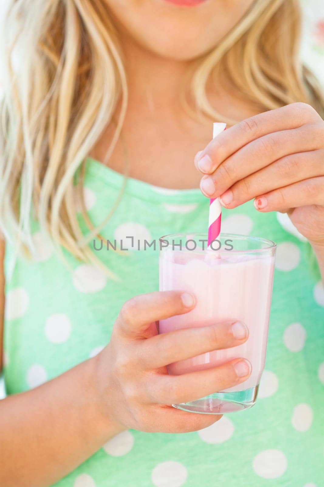 Closeup of glass of smoothie drink with straw held in hand by young girl