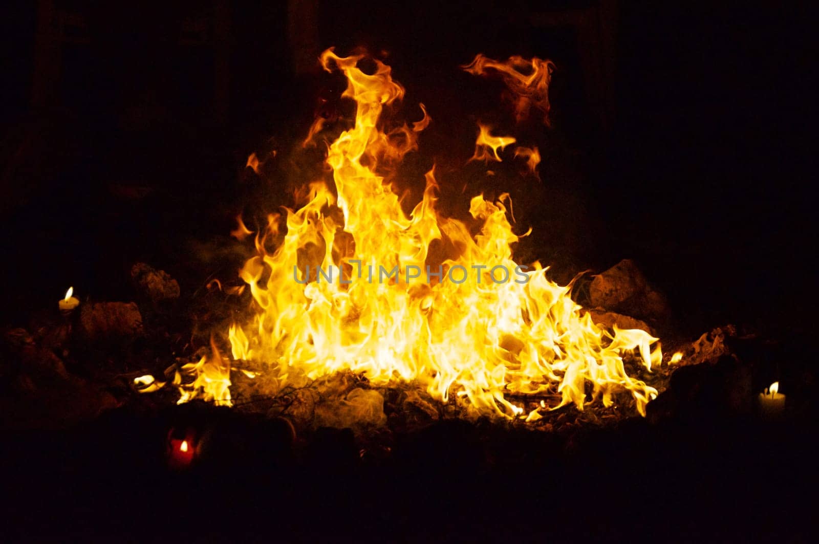 Flames and smoke fill this image of a ceremonial fire during a mayan ritual with a candle in each direction.